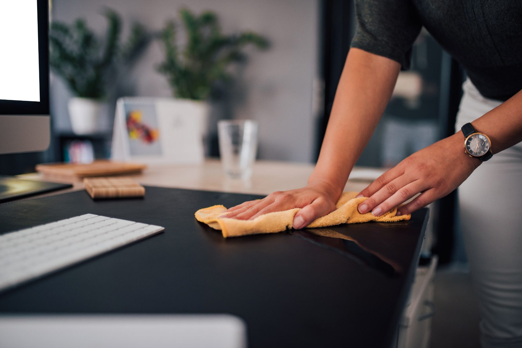 Cleaner wiping down a desk beside a keyboard in an office