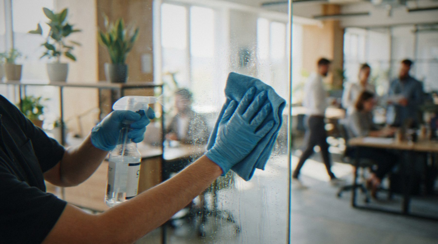 Cleaner wiping down a glass office partition after hours